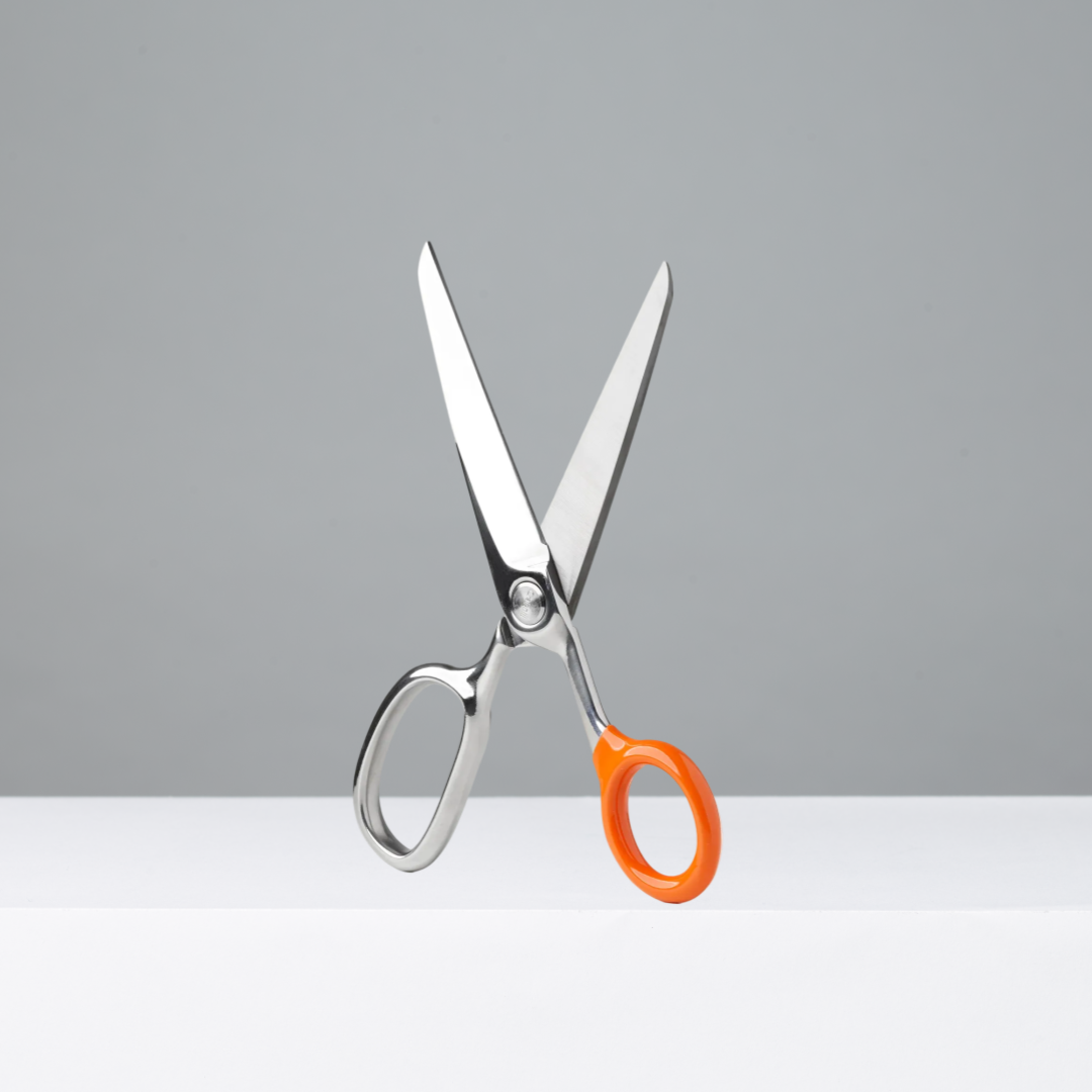 Scissors with orange handle on a white surface against a gray background