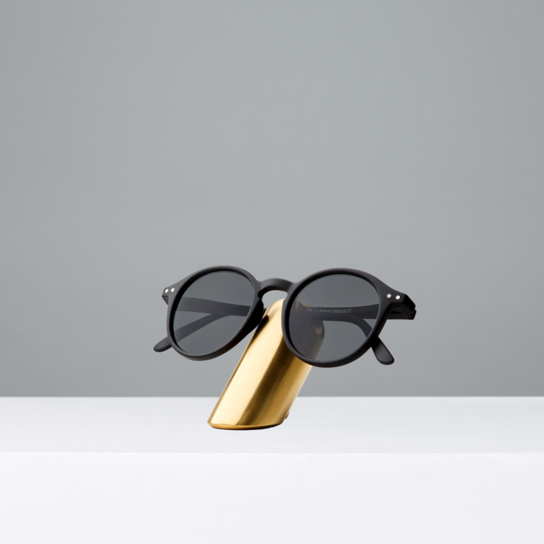Black sunglasses on a brass stand against a gray background