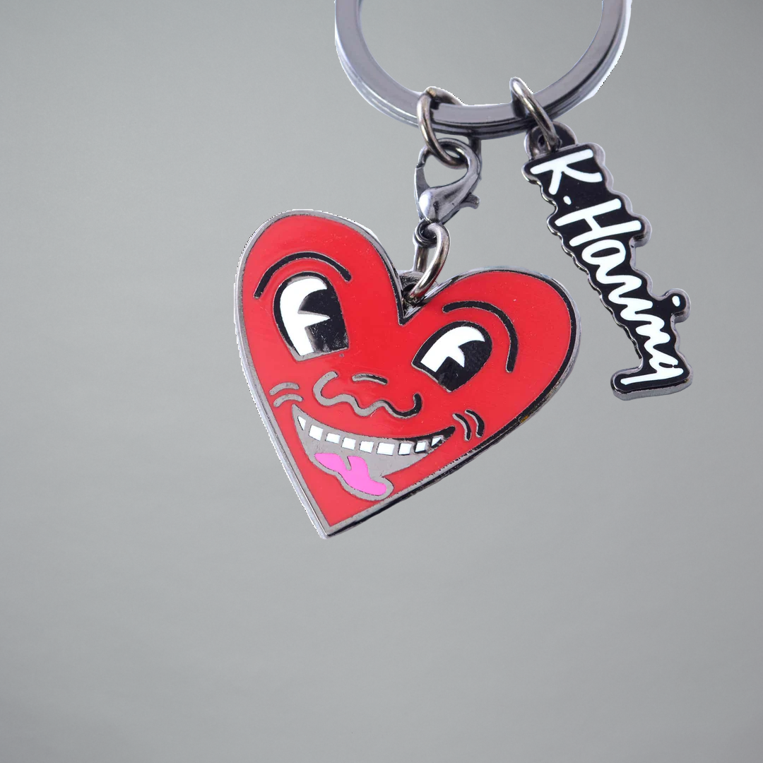 Keychain with a red Keith Haring heart-shaped charm featuring a face and a tag on a gray background