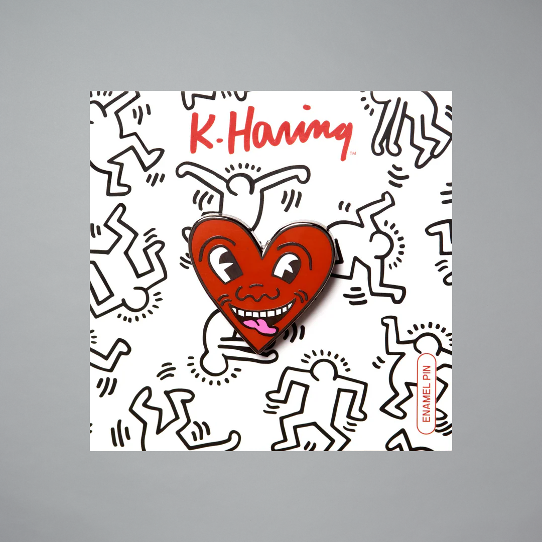 Keith Haring heart-shaped pin with a smiling face design on a gray background