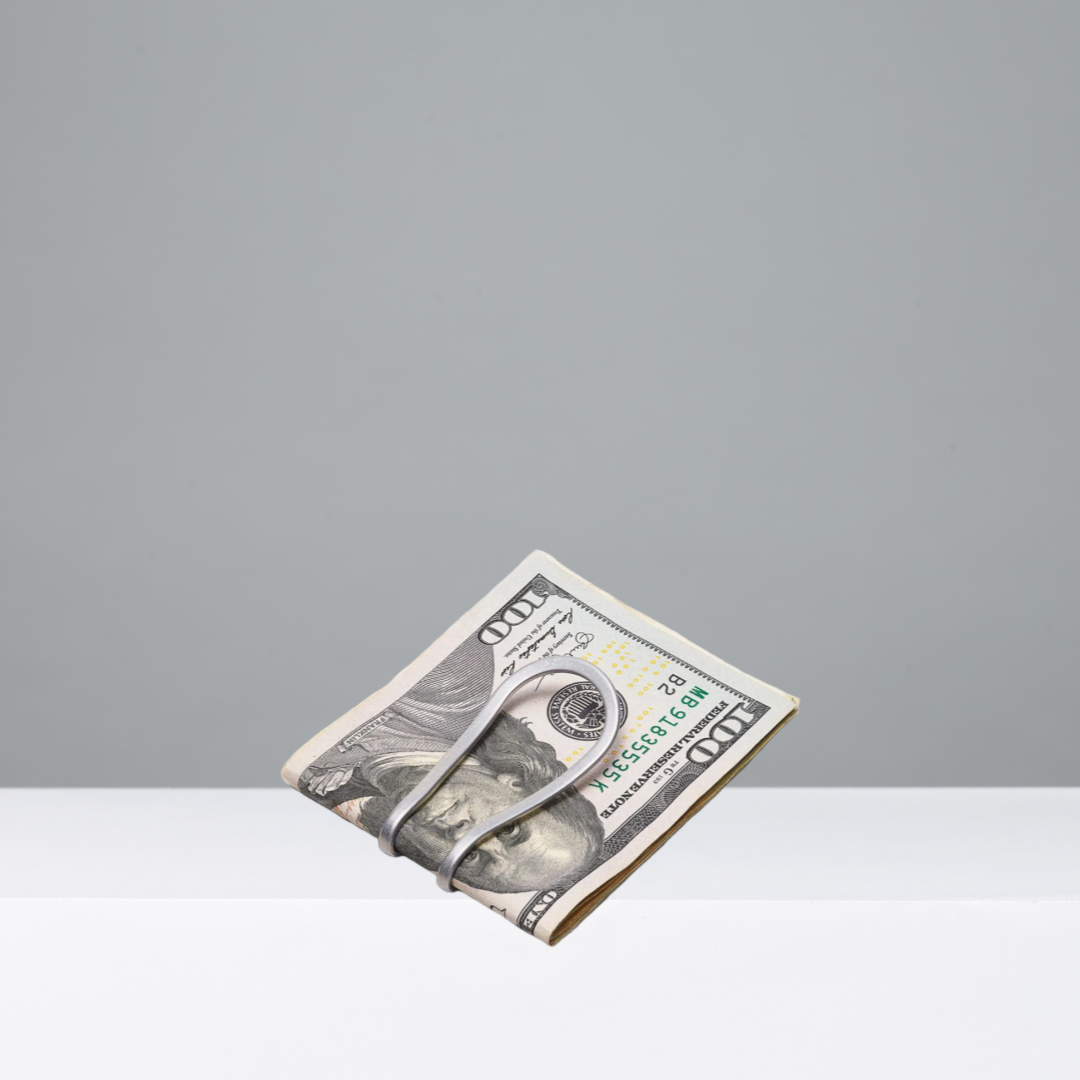 Silver money clip holding a folded bill on a gray background