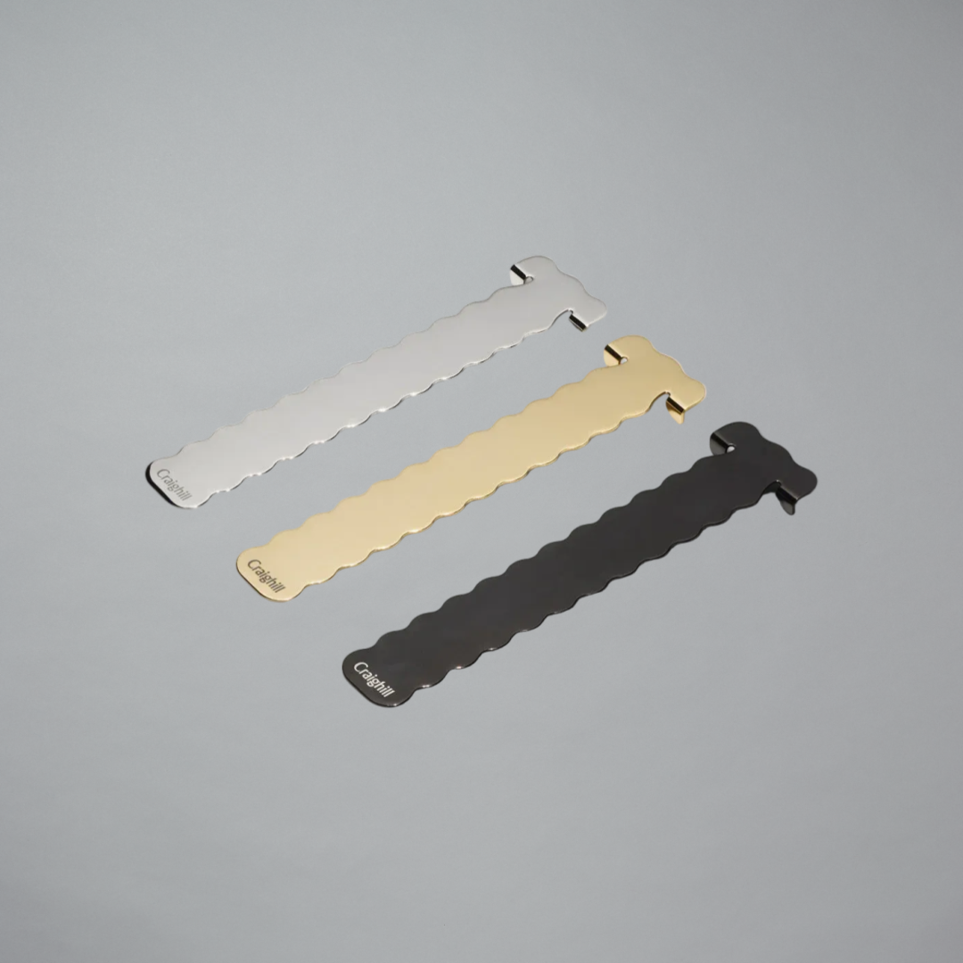 Three metal bookmarks in silver, gold, and black on a gray background