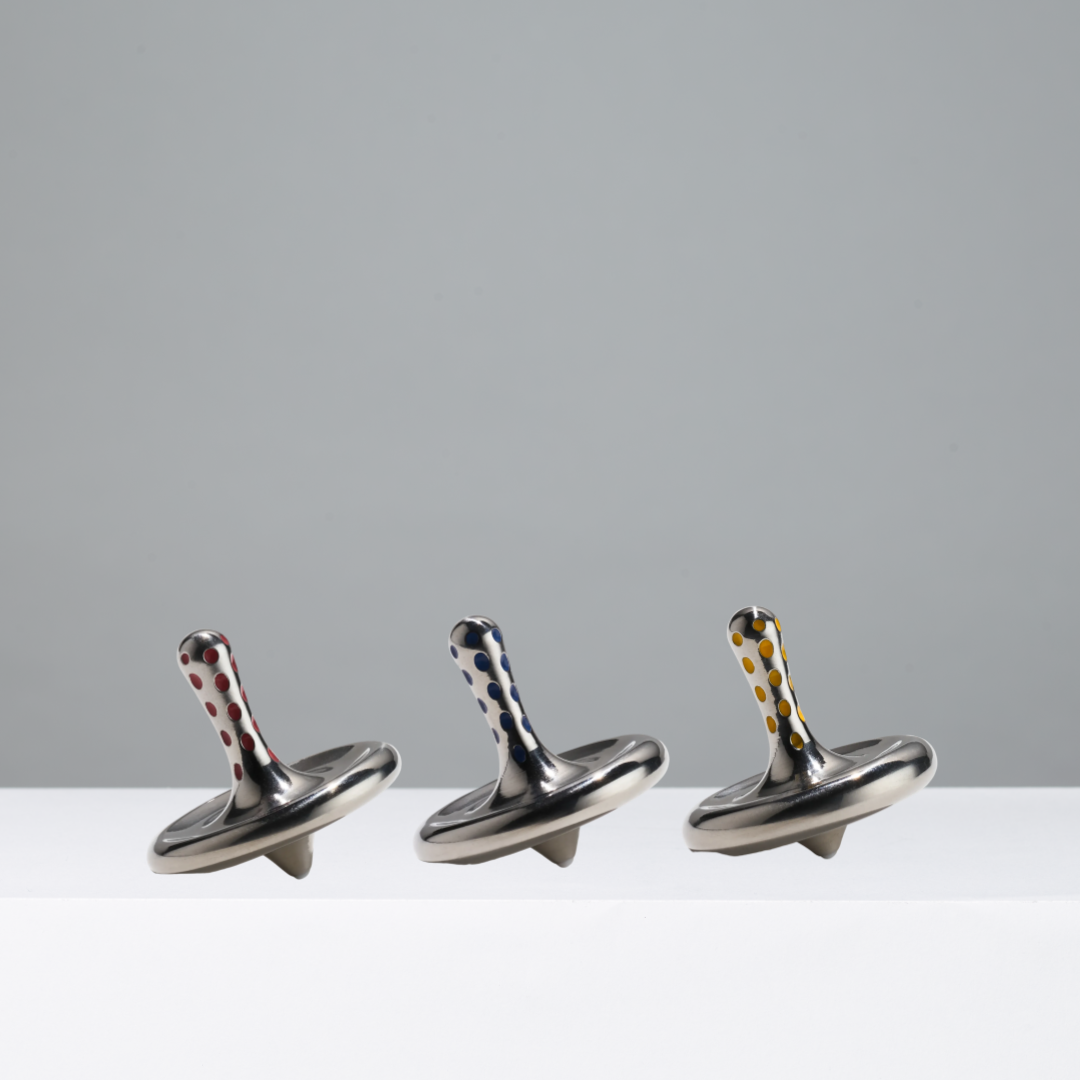 Three metallic spinning tops with decorative ends on a white surface and gray background