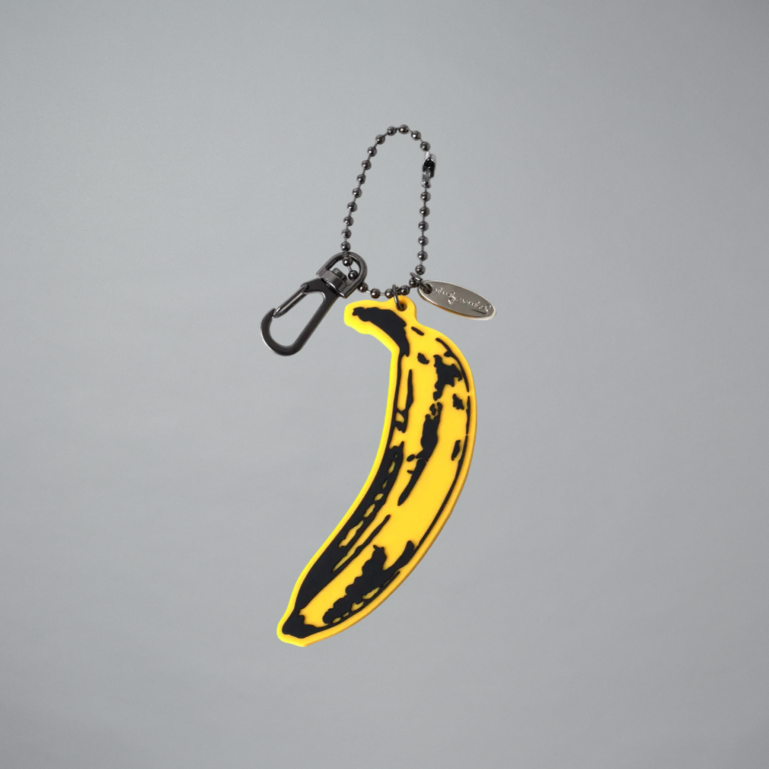 Keychain shaped like a yellow banana with black spots on a gray background