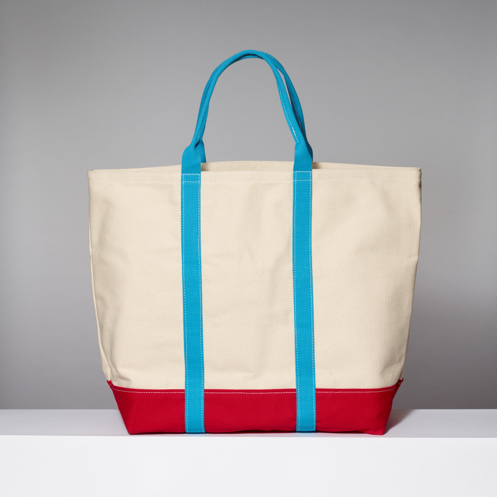 Beige tote bag with blue handles and red bottom section on a gray background
