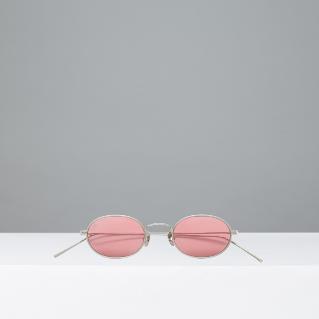 Pink round sunglasses on a white surface with a gray background