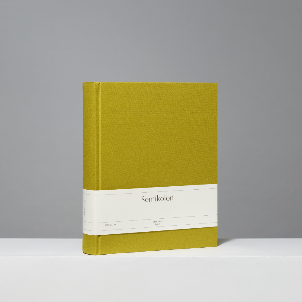 A hardcover photo album with a textured matcha linen cover and a white paper band around the middle. The band is printed with the title 'Semikolon' in black serif text.