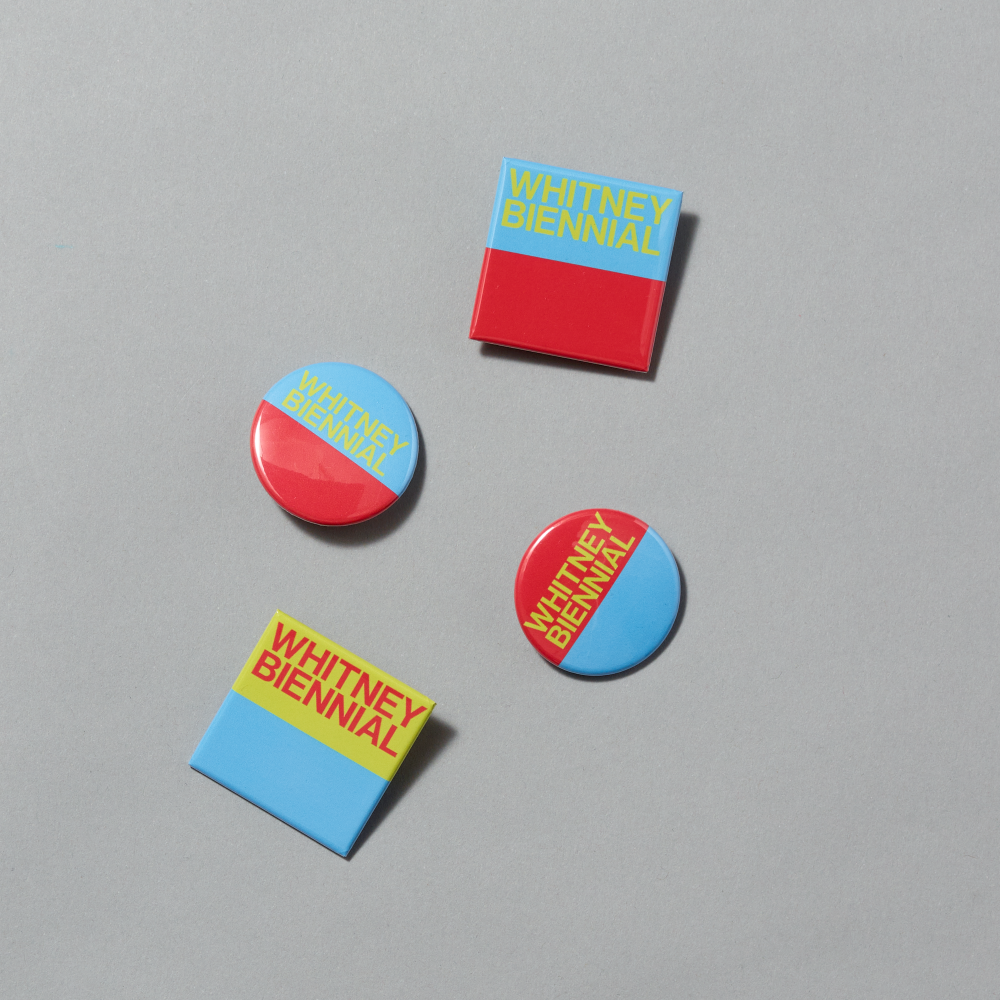 Set of four enamel pins in blue, red, and yellow colors displaying Whitney Biennial across each on a gray background