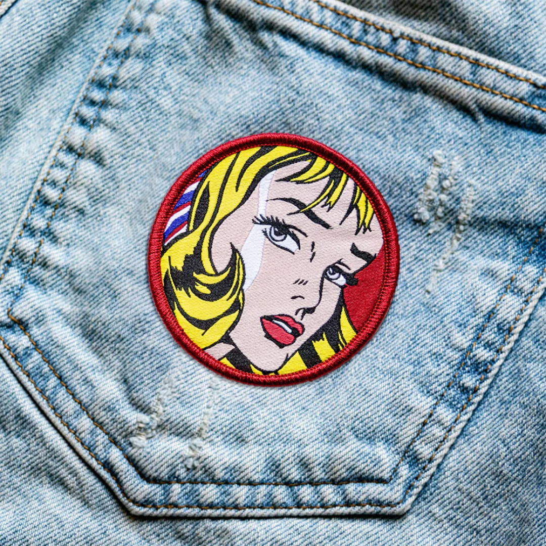 Embroidered patch featuring Girl with Hair Ribbon by Roy Lichtenstein ironed onto a pair of denim jeans