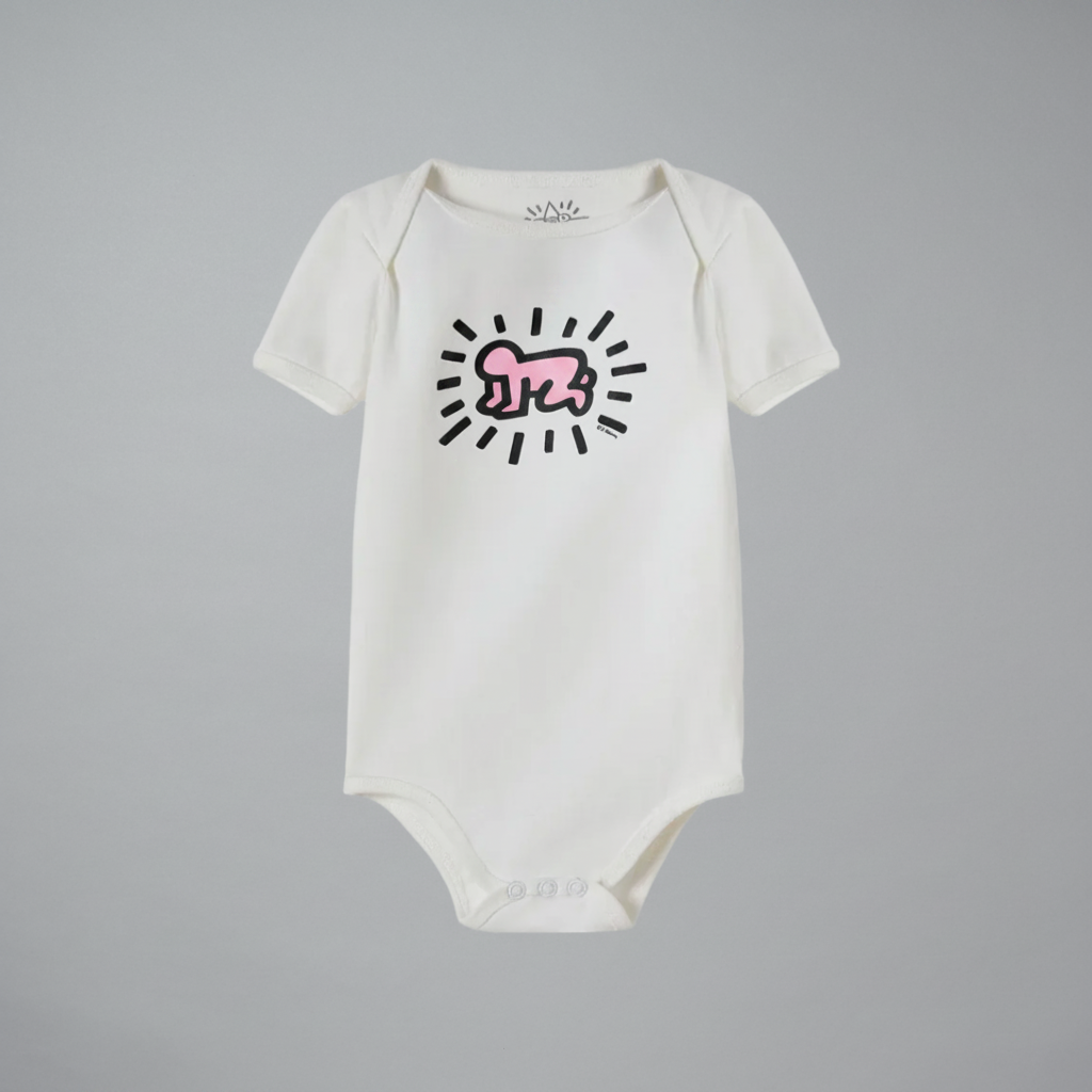 An off-white short-sleeve baby bodysuit featuring a pink and black Keith Haring style graphic on the chest, displayed against a neutral gray background.