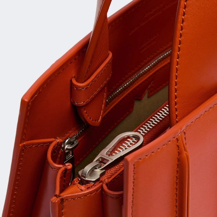 Close-up of an orange leather bag with a silver zipper pocket on a white background