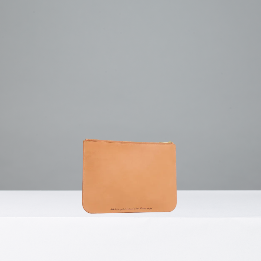 A tan leather wallet with a gold zipper and small black text at the bottom, photographed on a clean gray background.