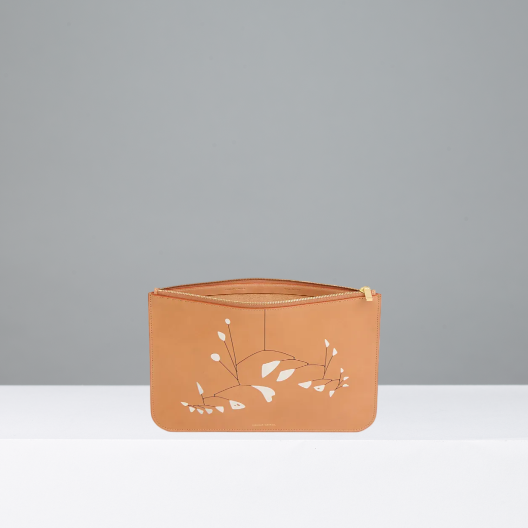 A tan leather zip wallet featuring Alexander Calder's 21 feuilles blanches on the front, set against a plain gray background.