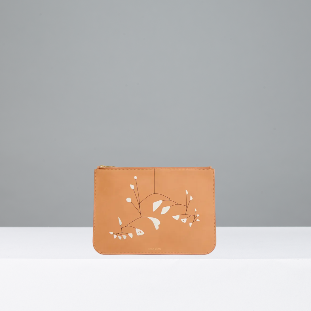A tan leather wallet with a gold zipper featuring Alexander Calder's 21 feuilles blanches on the front, displayed on a white surface against a gray background.