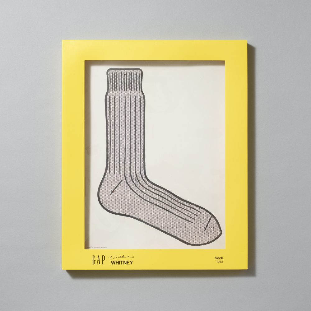 A yellow matte box containing a depiction of Roy Lichtenstein's work Sock on light gray background. The frame includes branding for GAP, Lichtenstein and Whitney at the bottom