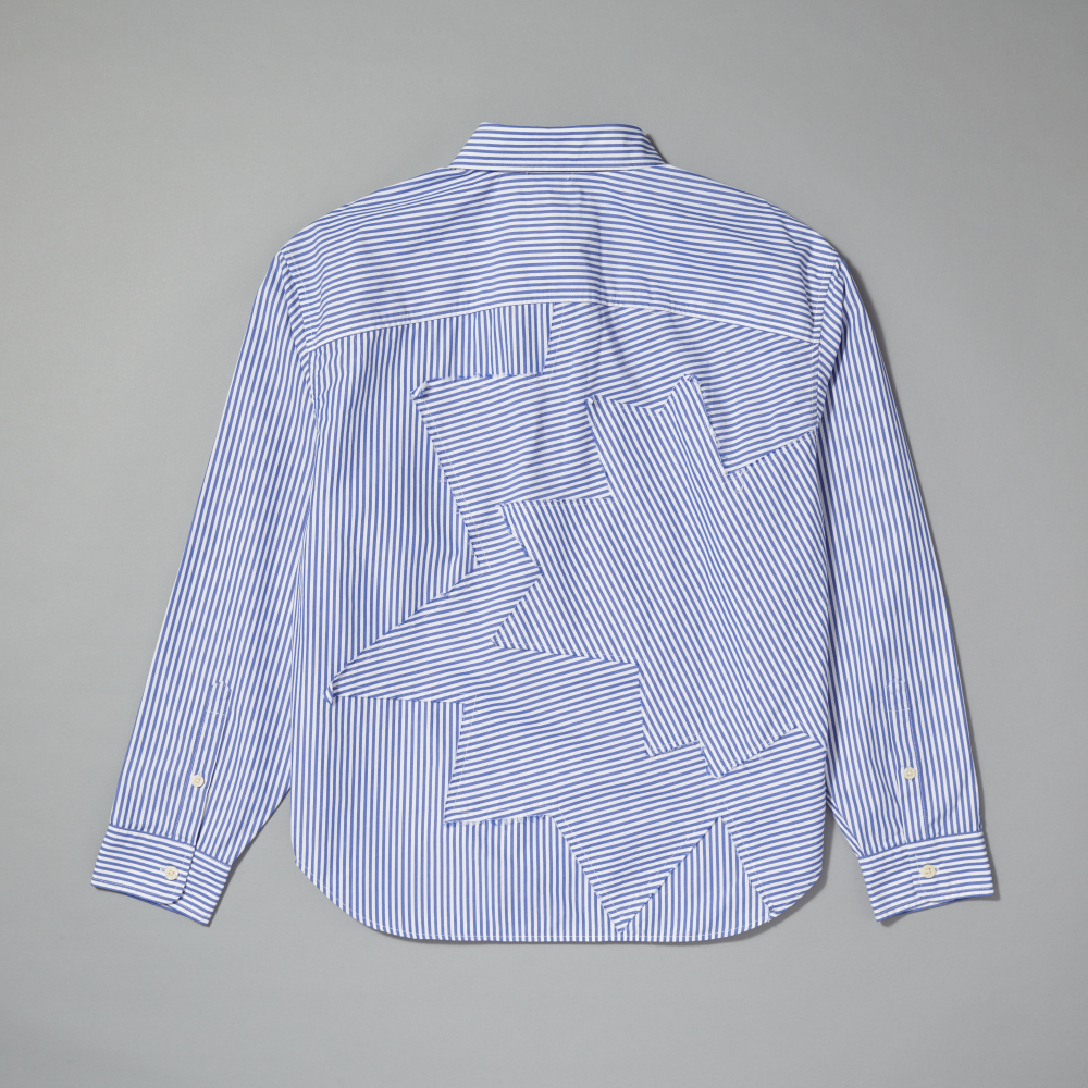 A long-sleeve button-up shirt shown from the back, featuring a blue and white striped pattern with a large abstract geometric patchwork design on the back panel inspired by Roy Lichtenstein's work Standing Explosion (Black) laid flat against a gray background