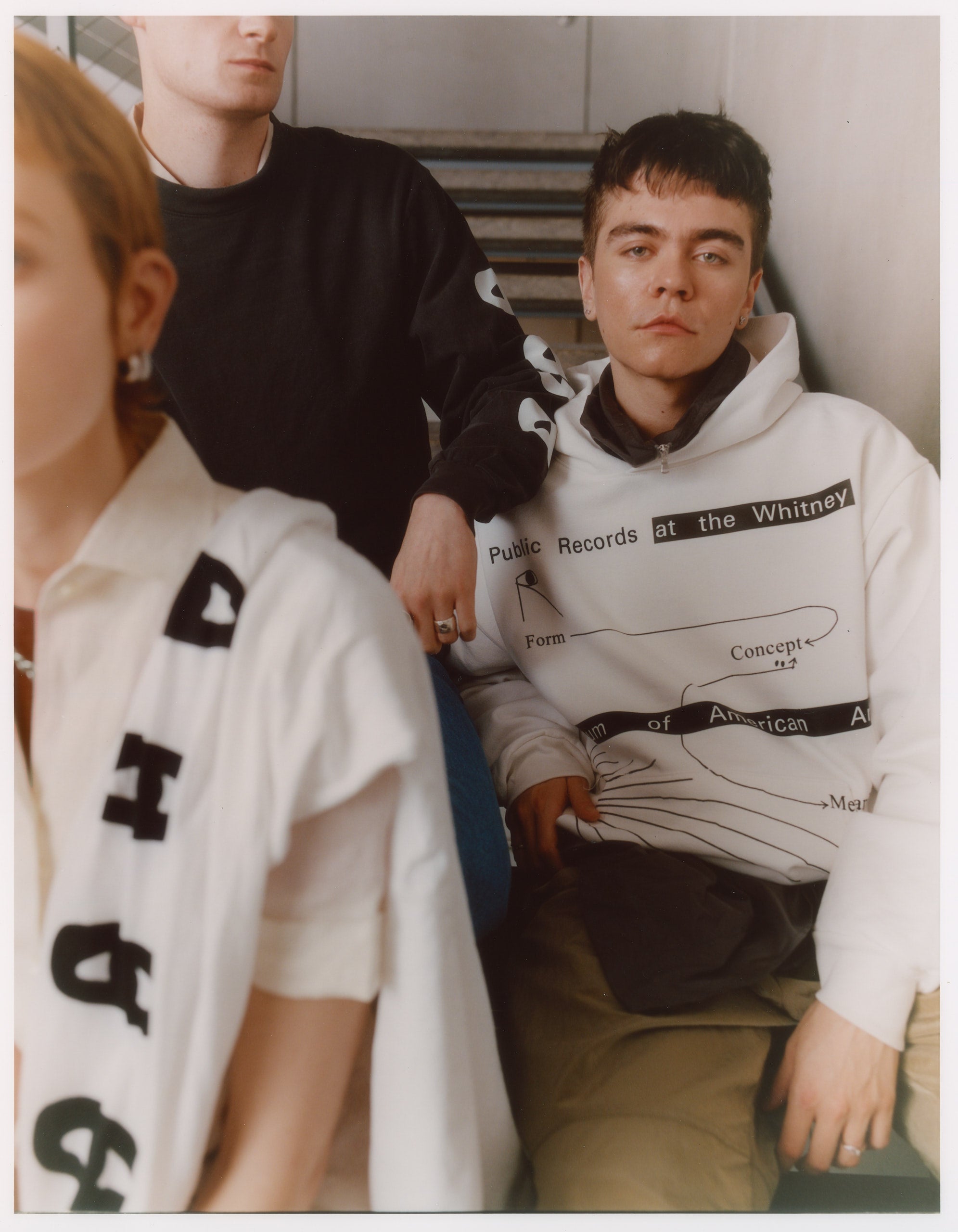 Model wearing 100% fleece white hoodie featuring Public Records at the Whitney Museum of American Art July 2024 to June 2025 in black text
