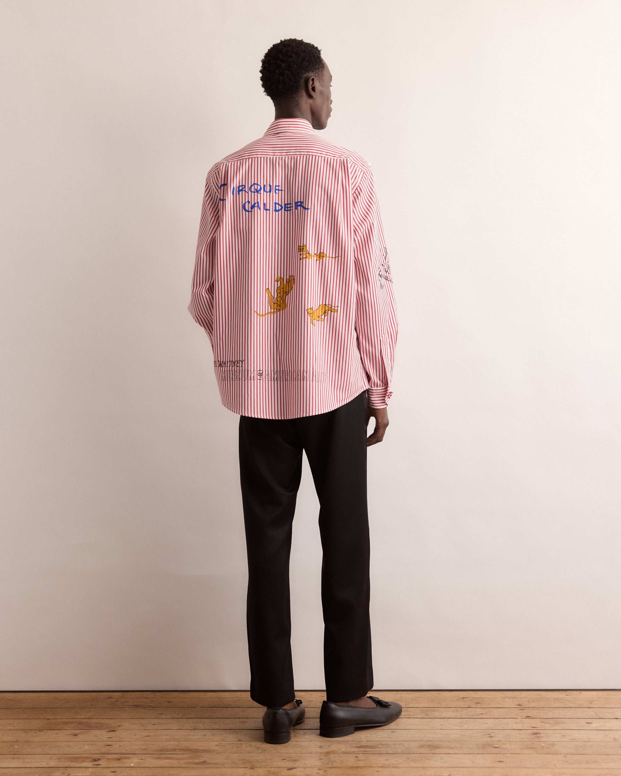 Person wearing a red and white striped shirt with text and graphics, standing against a plain background