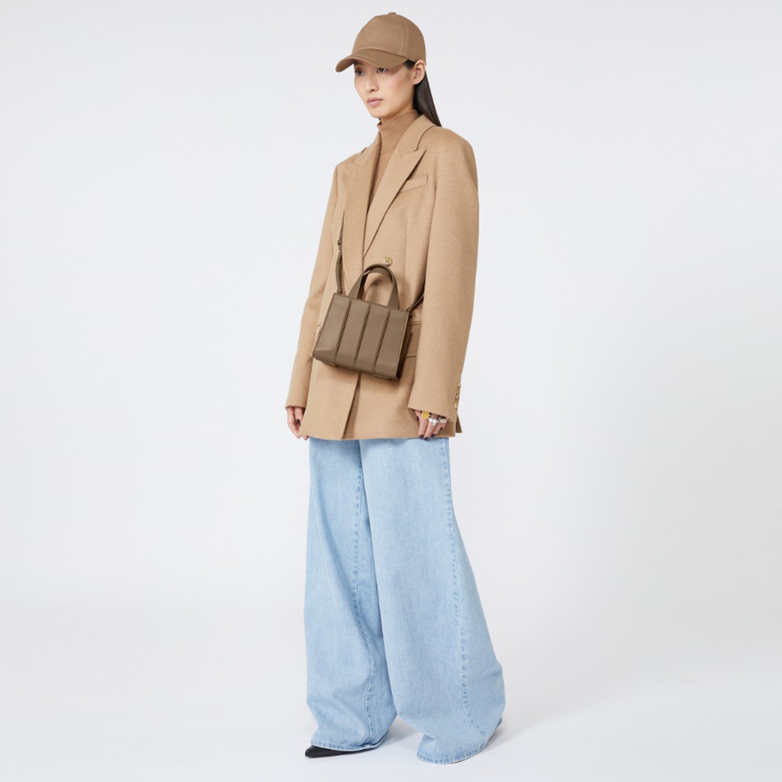 Model wearing a beige coat, light blue jeans, and a beige cap on a white background