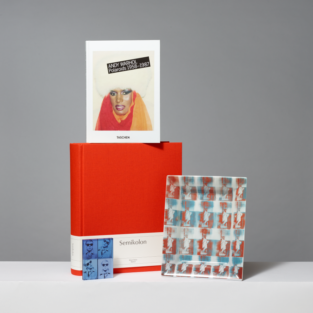 Assortment of Warhol inspired products including Andy Warhol Polaroids 1958-1987, Semikolon Classic Medium Photo Album, a Ligne Blanche porcelain tray featuring Statue of Liberty, and a self portrait magnet by Pintrill.