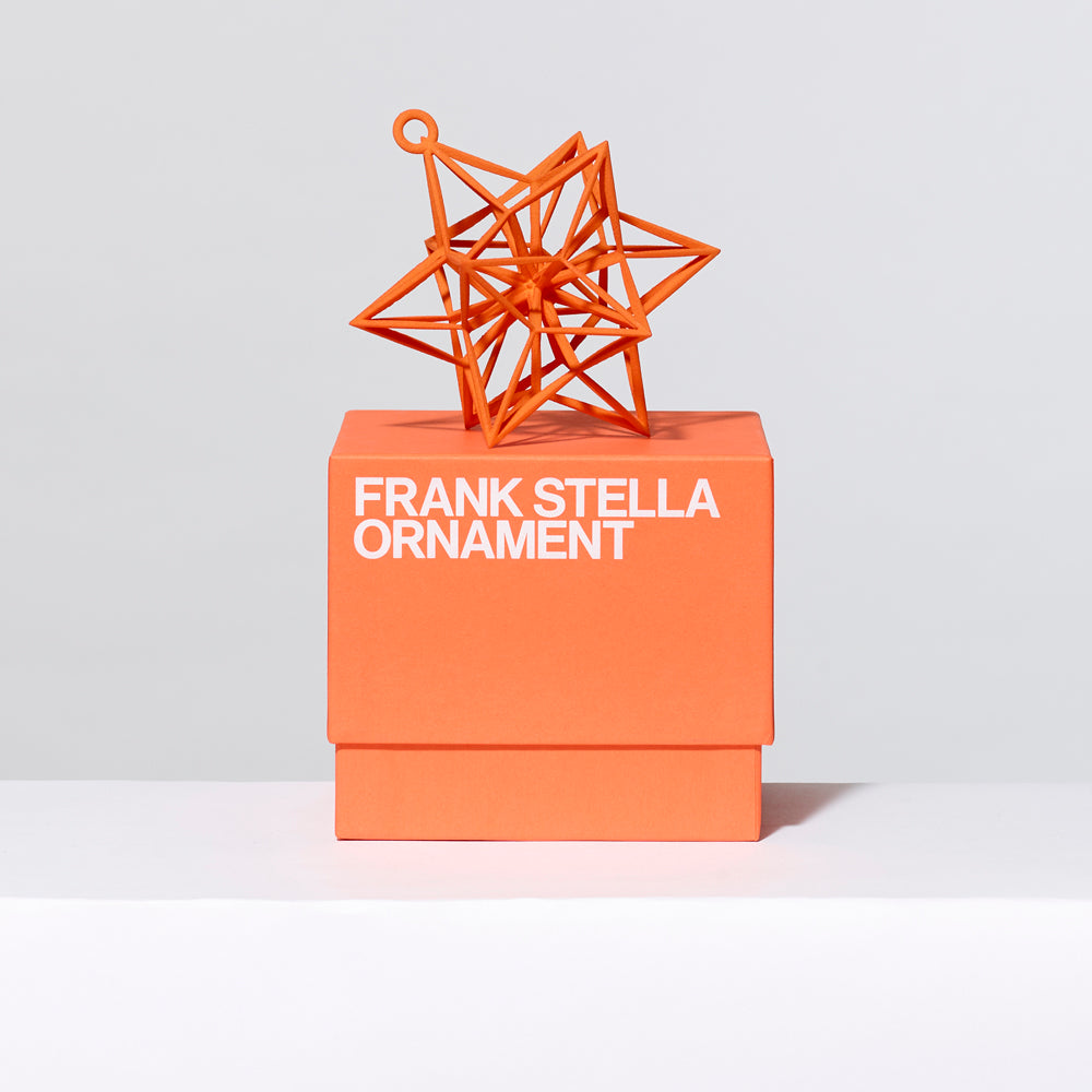 3-D printed plastic Frank Stella star ornament in orange on top of gift box. Measures approximately 4" x 4" x 4"