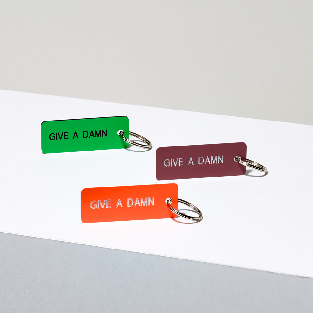Assortment of etched acrylic keychains in various colors featuring the text "Give A Damn"