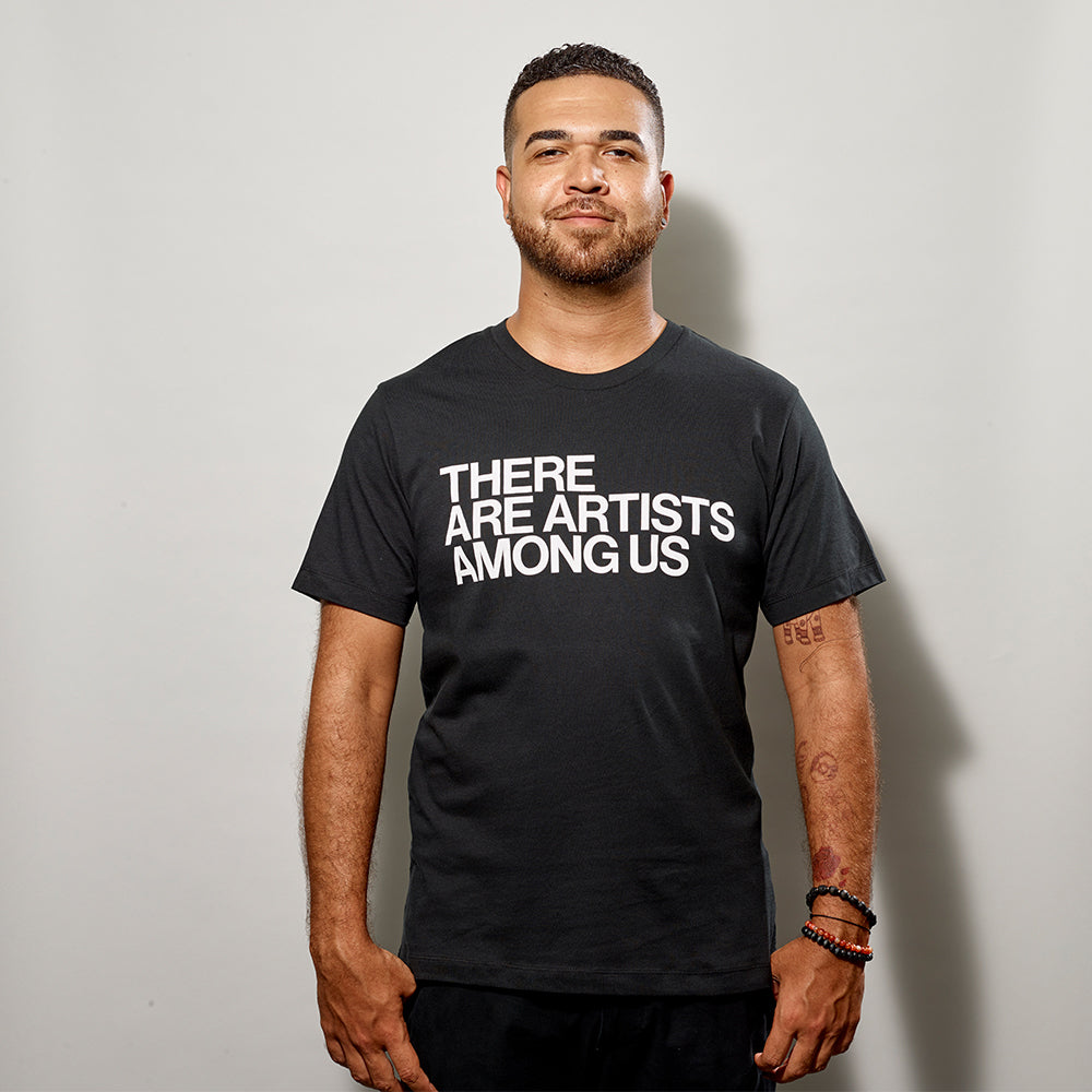 Model wearing a black t-shirt that says There Are Artists Among Us in white text