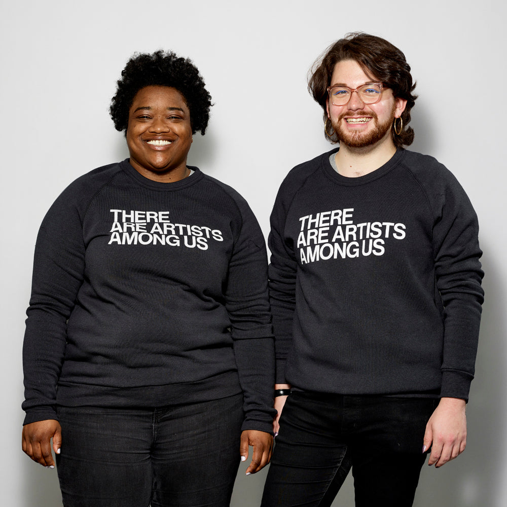 Two models wearing the Cotton/Polyester blend black sweatshirt with There Are Artists Among Us written across in white text.