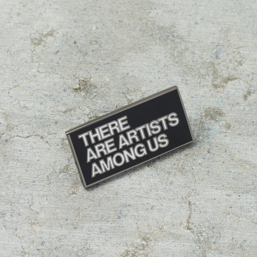 Black nickel plated brass and hard enamel pin that reads There Are Artists Among Us