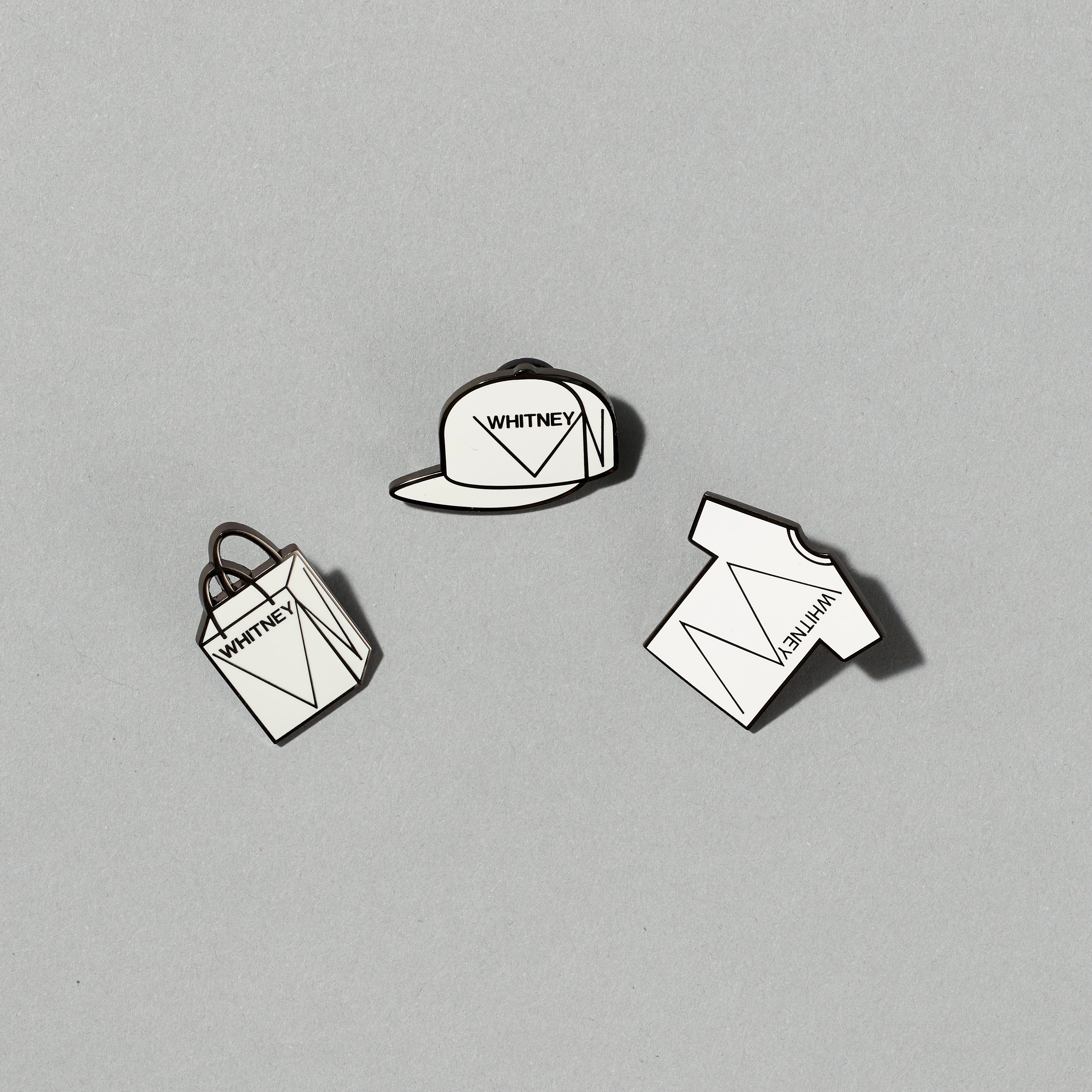 Set of three Black nickel plated brass with hard enamel pins featuring Whitney shopping bag, Whitney cap, and Whitney t-shirt