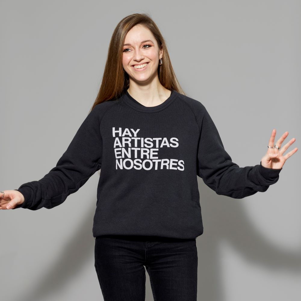 Model wearing black Cotton/Polyester blend sweatshirt with "Hay Artistas Entre Nosotres" text in white across