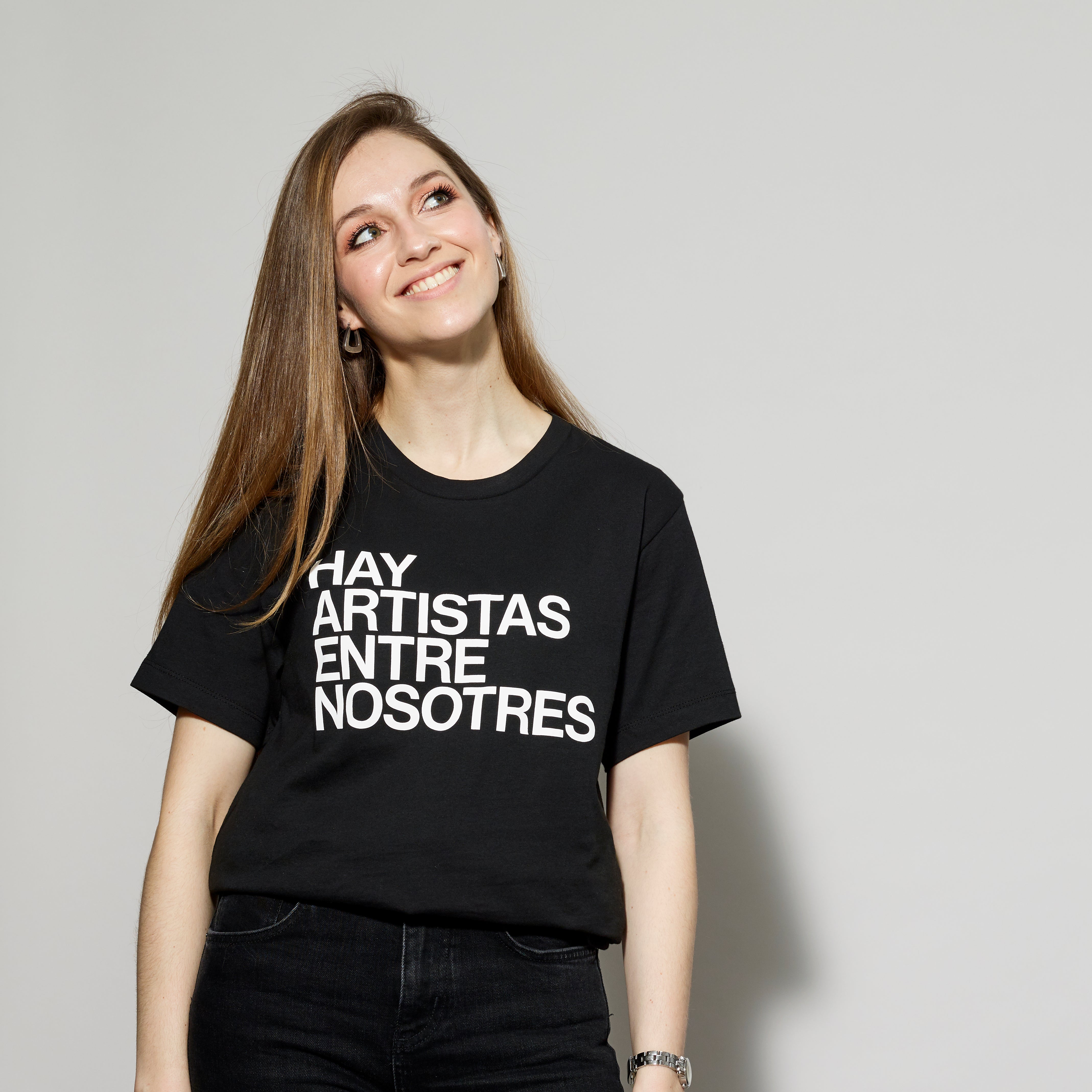 Model wearing 100% cotton black t-shirt with Hay Artistas Entre Nosotres screen printed in white text
