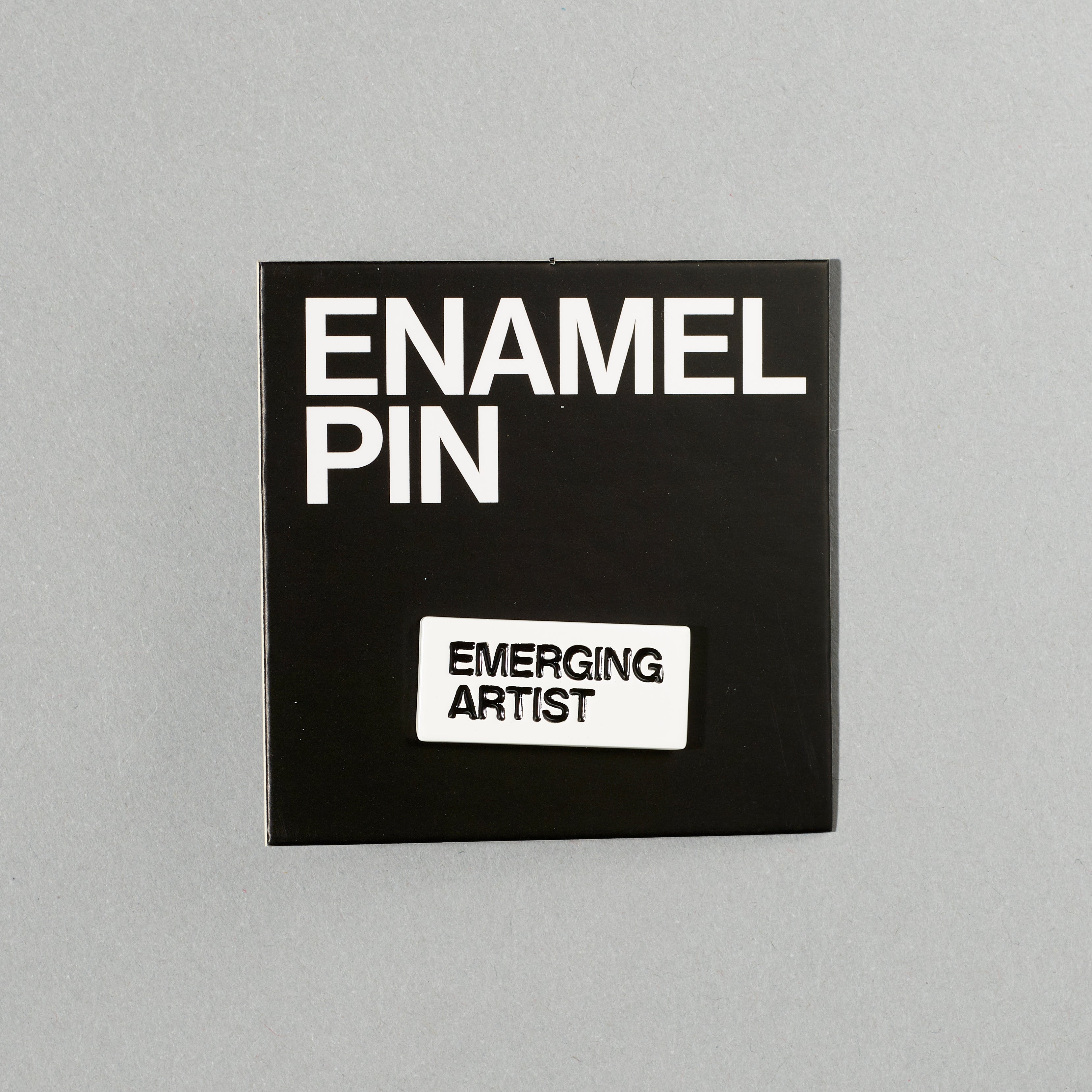 Black nickel plated brass and hard enamel pin that reads Emerging Artist