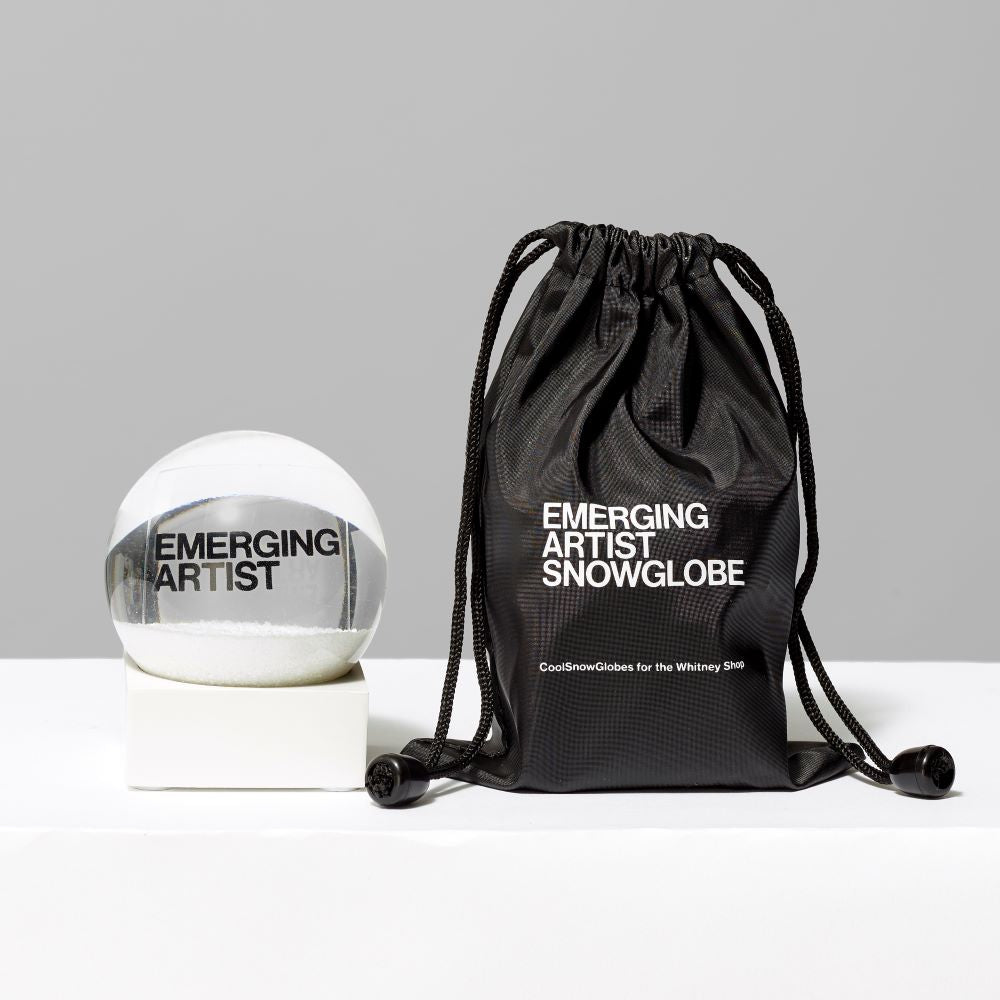 3 Fl oz. and 2.56" Snow Globe featuring the text "Emerging Artist" standing next to an accompanying black pouch that reads "Emerging Artist Snow Globe"