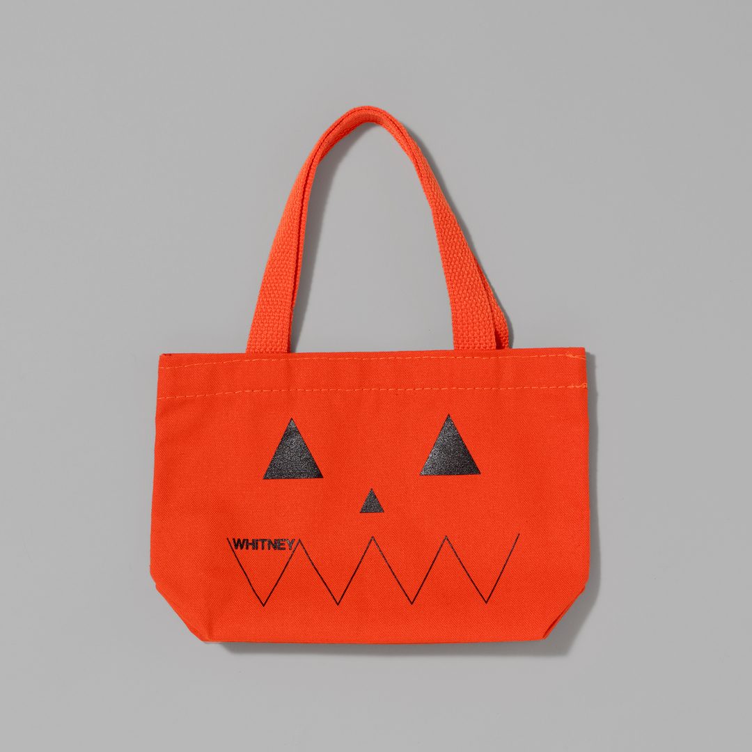 Orange tote bag with pumpkin face design on a gray background