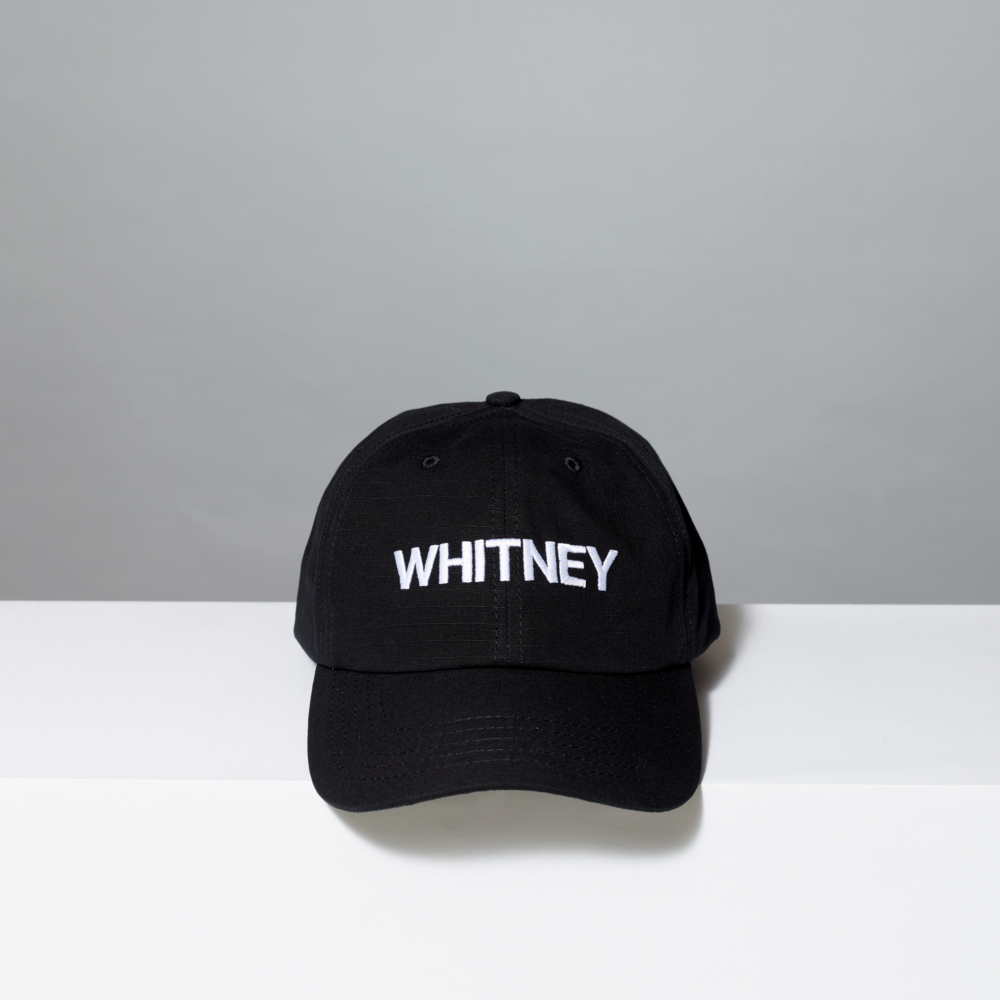 Black cap with 'WHITNEY' text on a white surface and gray background