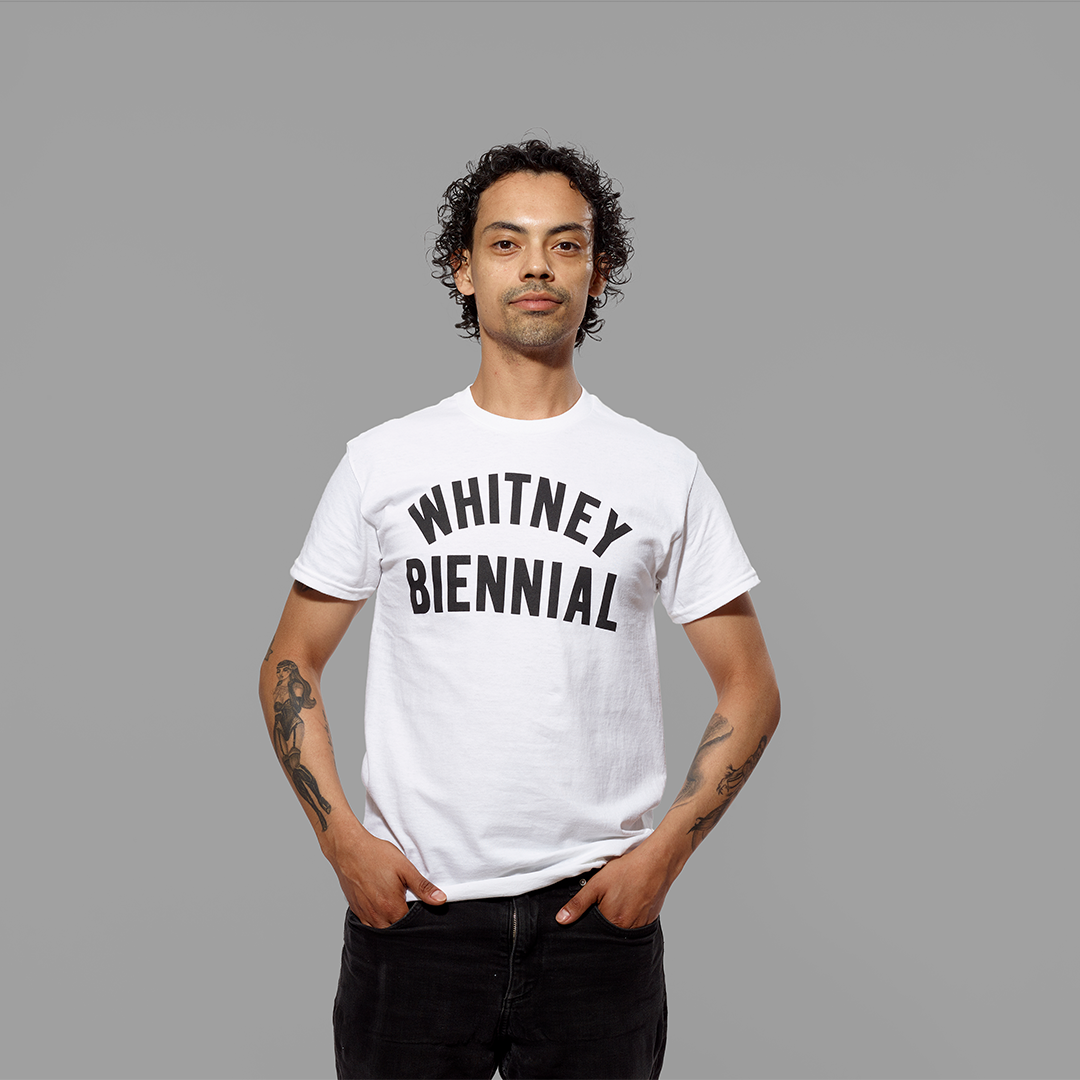 Model wearing a 100% cotton white t-shirt with Whitney Biennial in black text