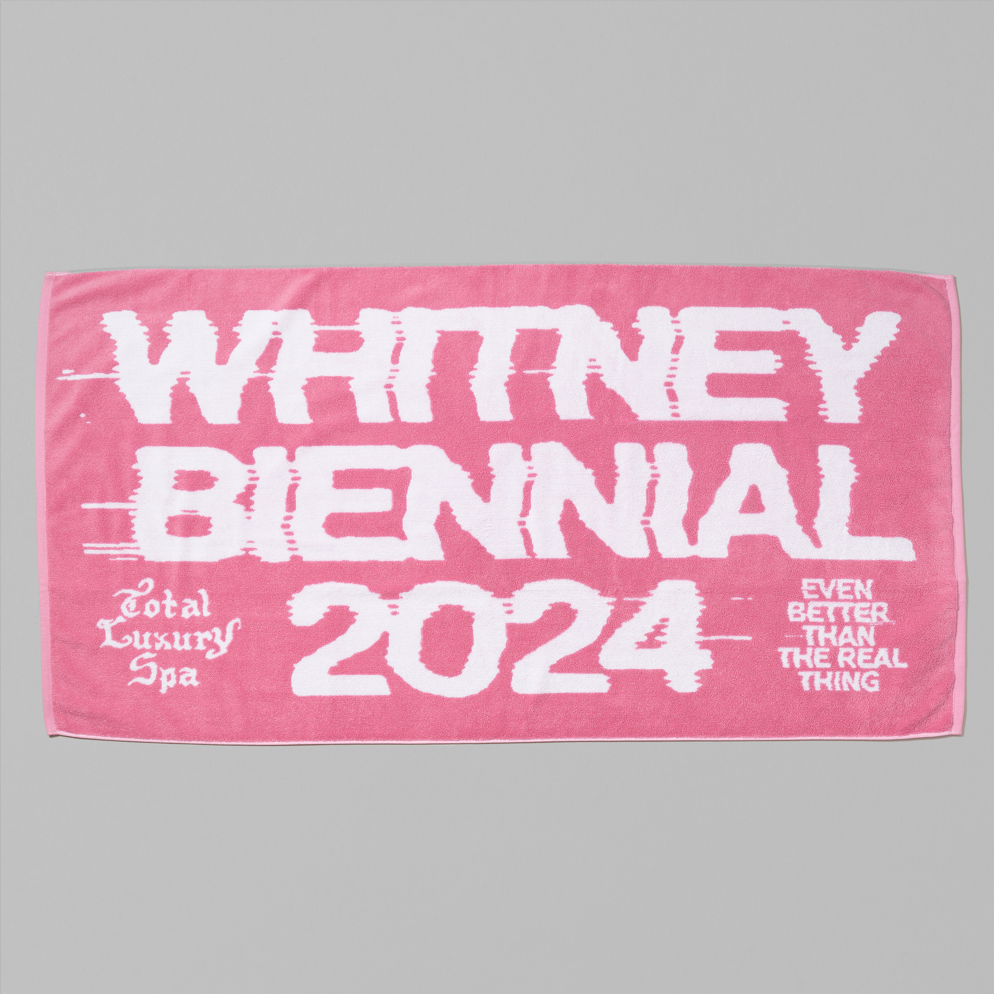 100% cotton pink beach towel with Whitney Biennial 2024 Even Better Than The Real Thing and Total Luxury Spa in white text. Measures 30" x 60"