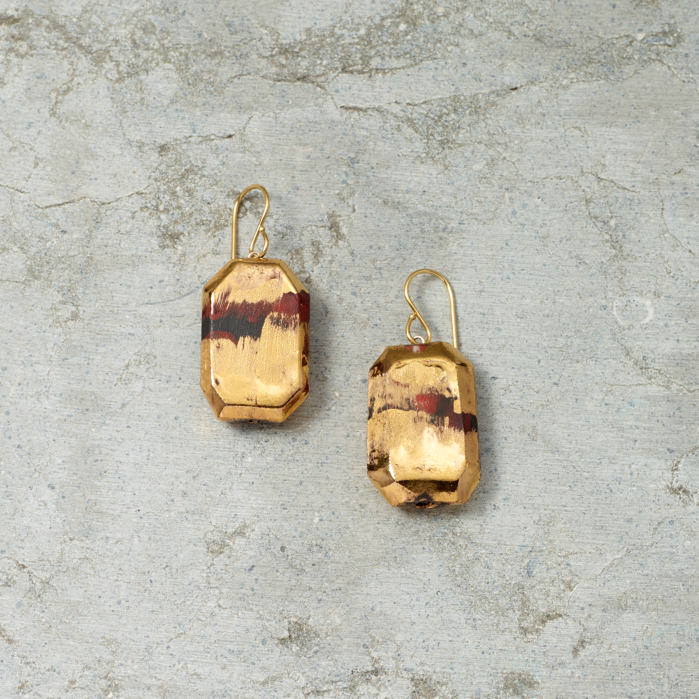 Gold earrings with a textured design on a gray stone surface