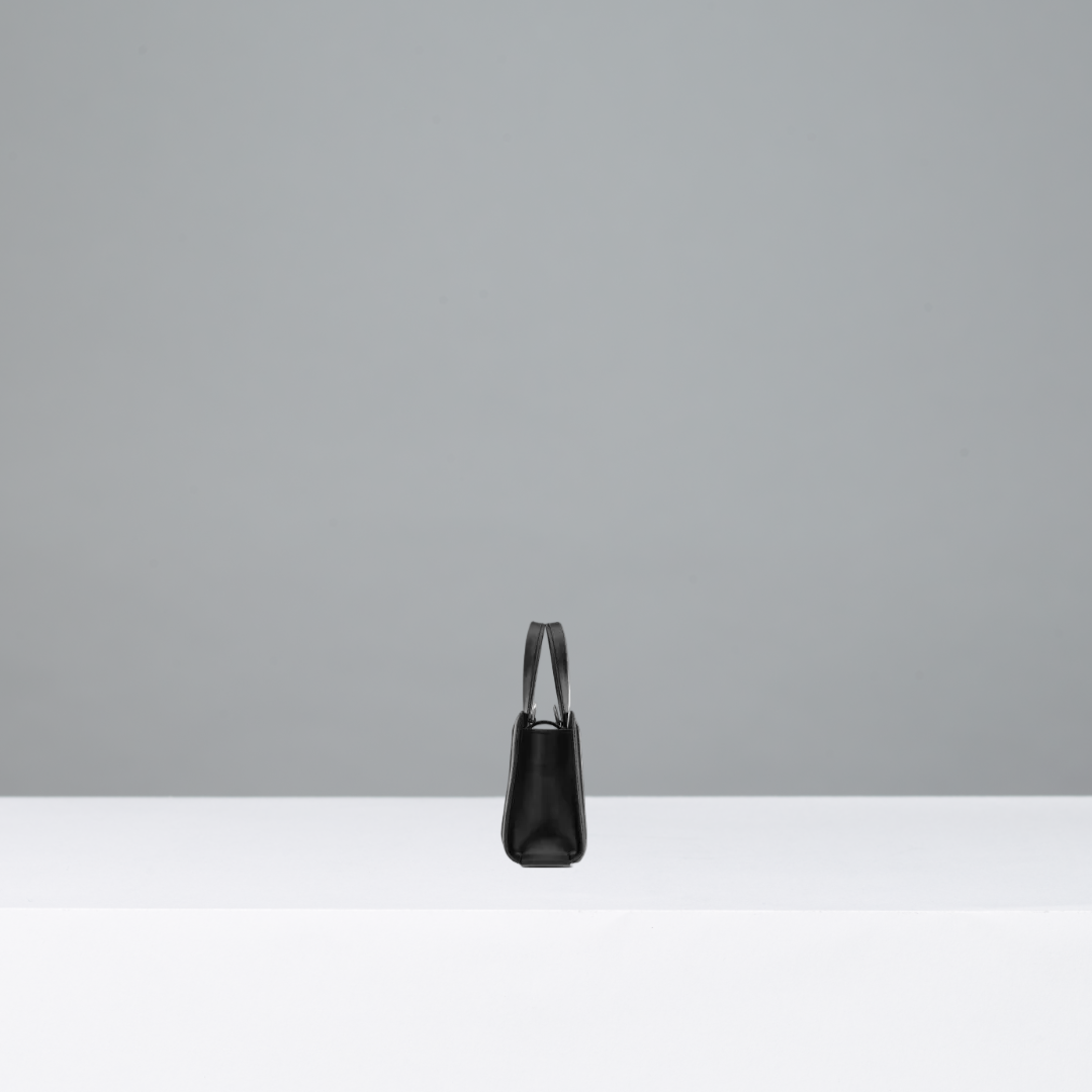 Black handbag on a white surface with a gray background