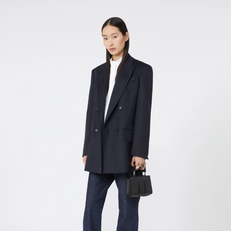 Model wearing a dark coat and jeans holding a black handbag on a white background