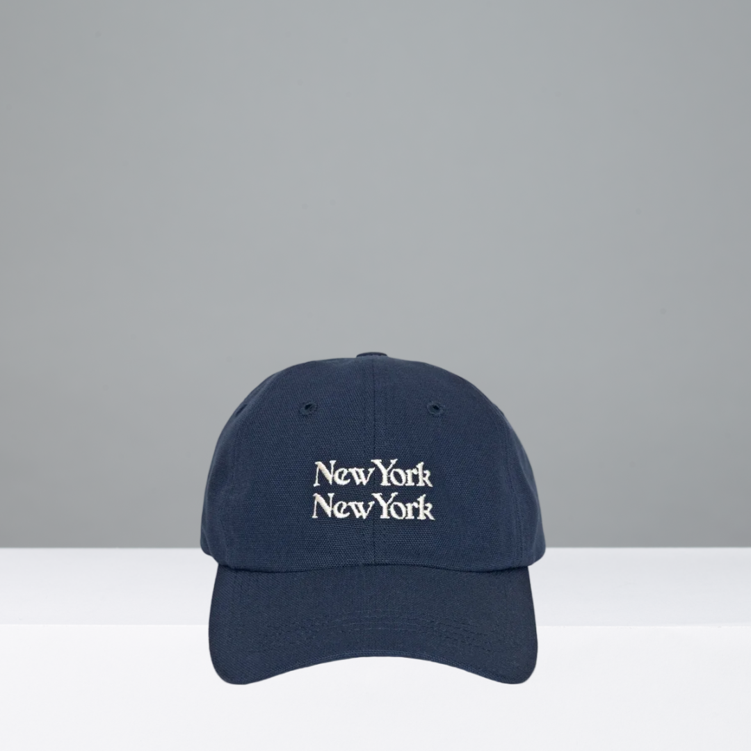 A navy blue baseball cap with 'New York New York' embroidered in white gothic-style lettering on the front, displayed against a neutral gray and white background.