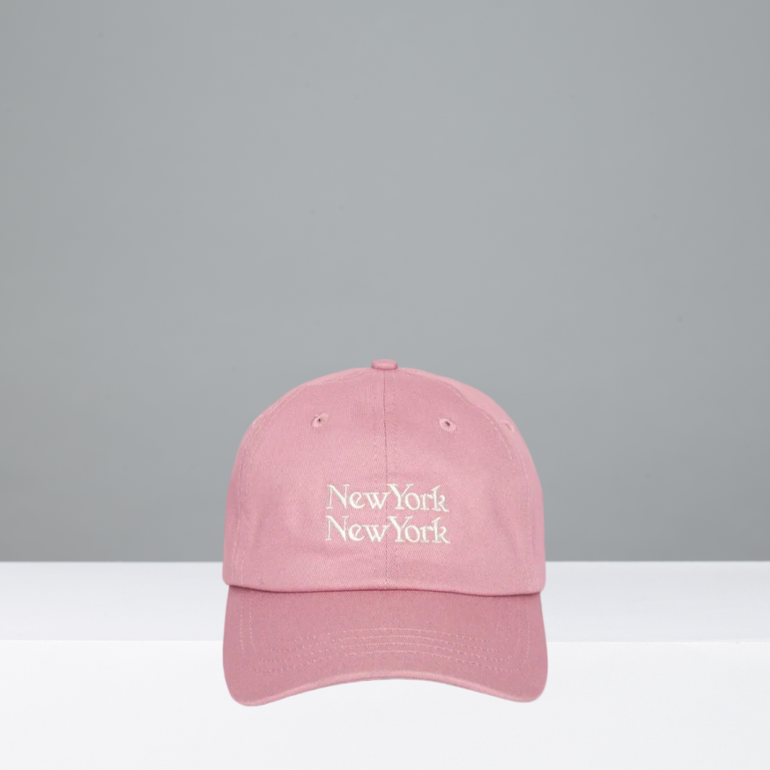 A pink baseball cap with 'New York New York' embroidered in white script on the front, shown against a plain gray background.
