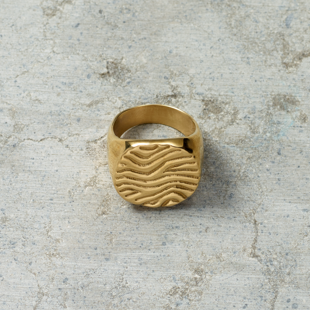 Gold ring with wavy design on a textured gray surface