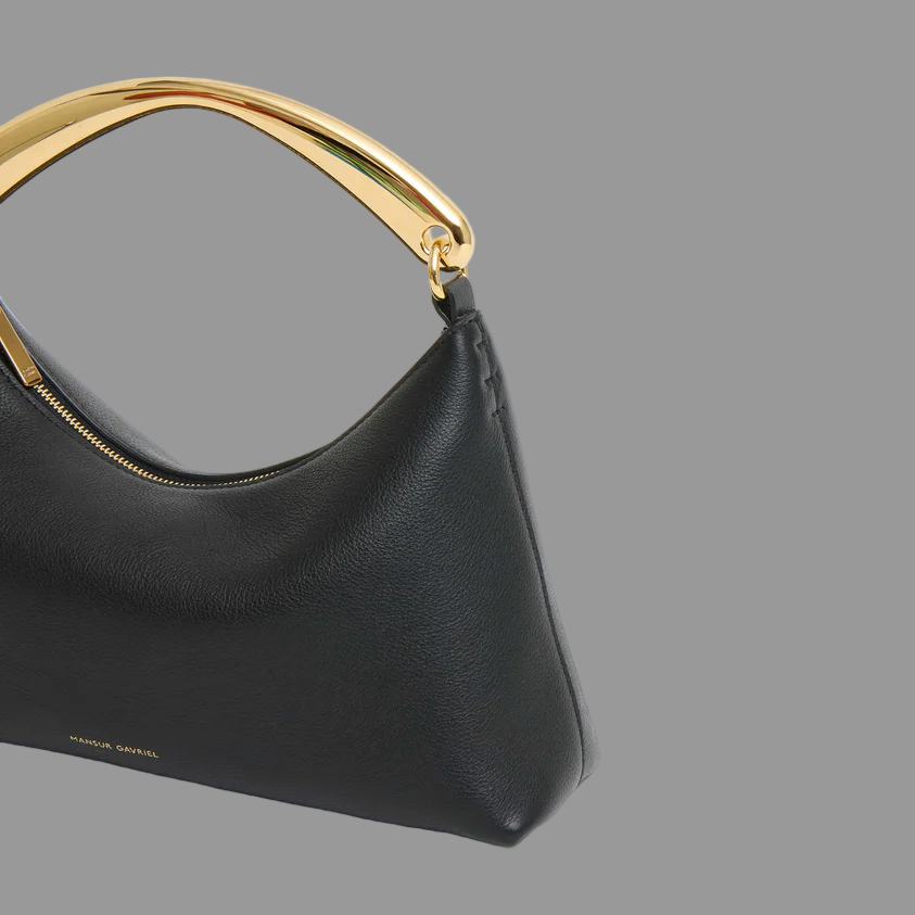 Black handbag with goldr metal handle on a gray background