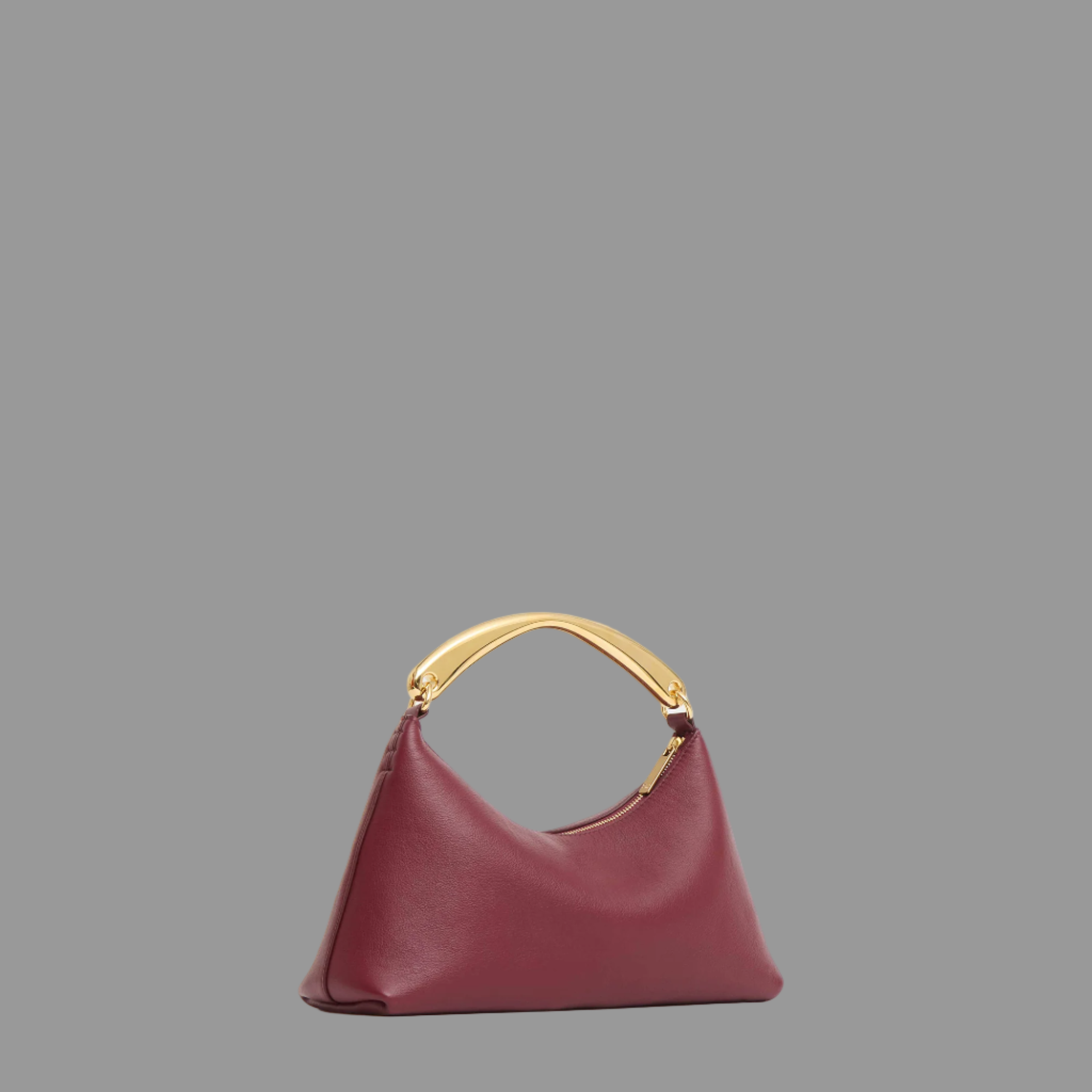 Oxblood handbag with gold handle on a light gray background