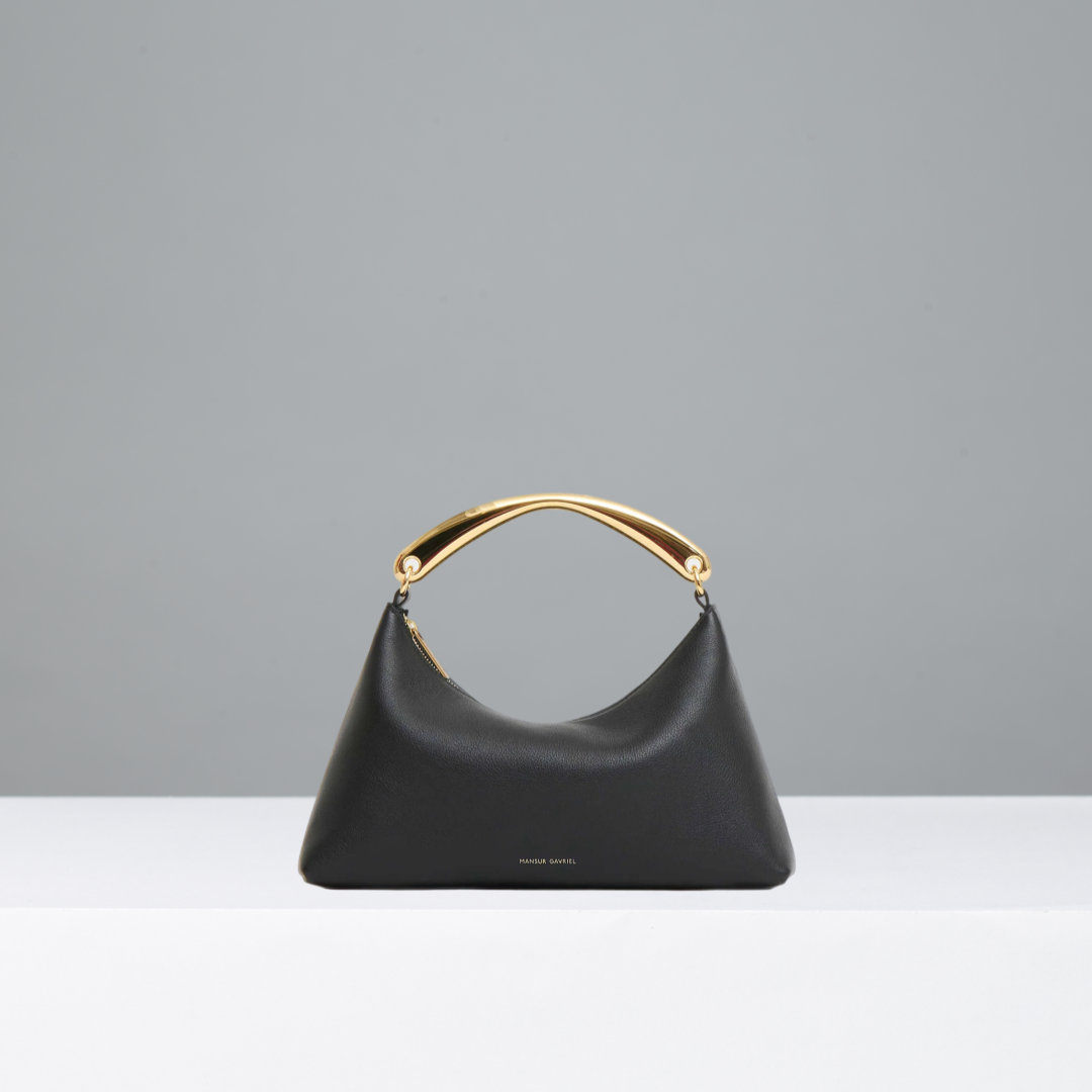 Black handbag with gold metal handle on a gray background