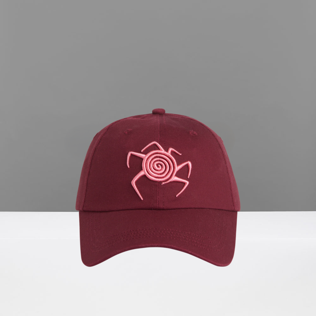 Maroon cap with pink spider design on a gray background