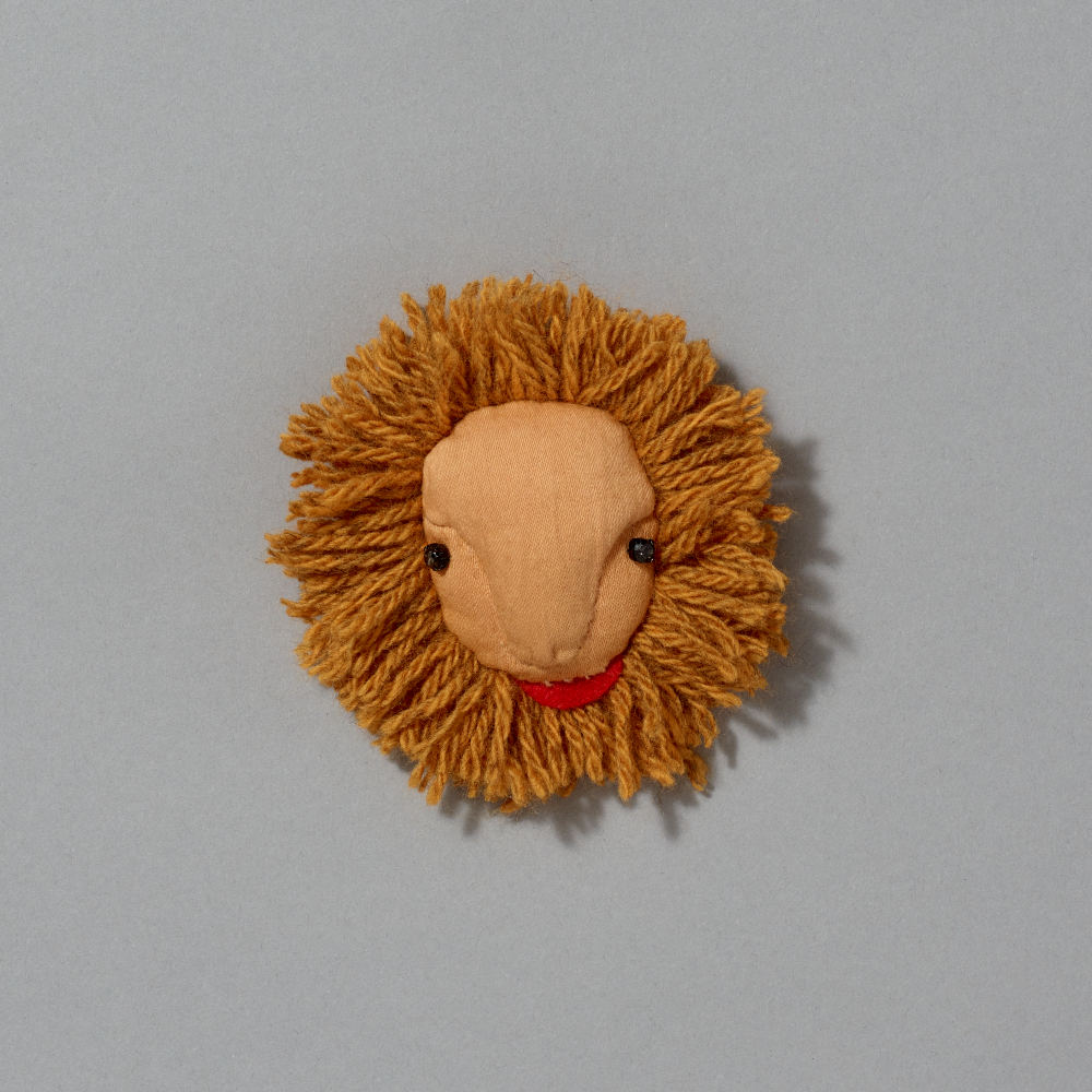 Small lion head brooch with a red tongue on a gray background