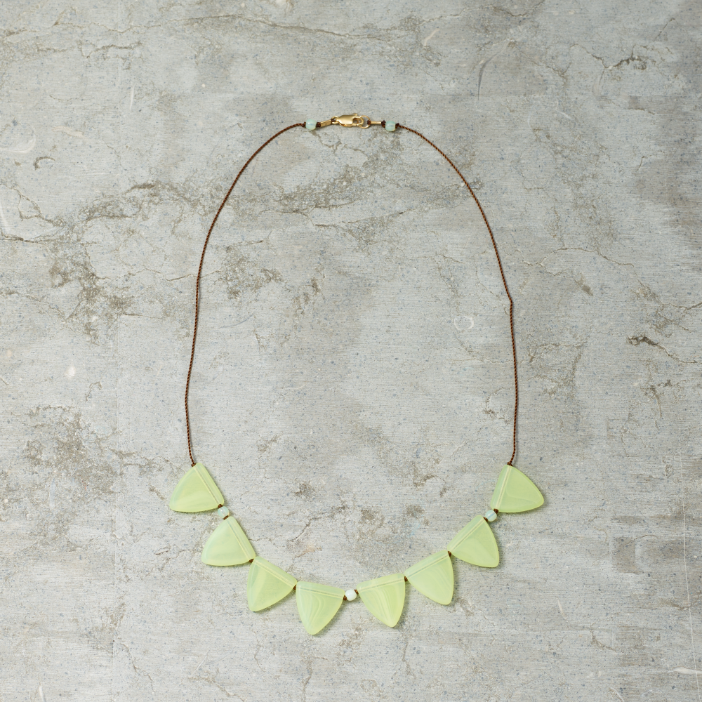 Necklace with light green triangular pendants on a gray surface